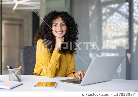 Portrait of a young successful businesswoman inside the office, office worker smiling and looking at the camera, satisfied woman working with laptop. 127828057