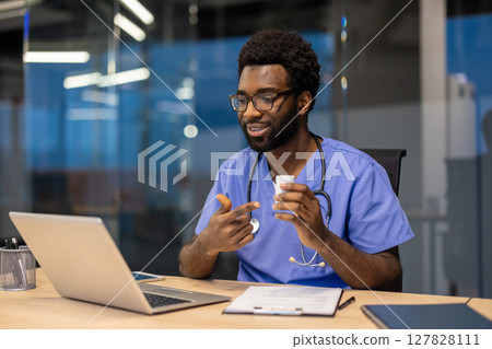 Online video consultation, experienced doctor in medical gown and with stethoscope works remotely inside office, uses laptop for video call, explains and consults patient. 127828111