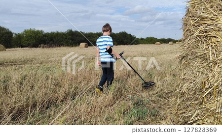guy with a metal detector is looking for a treasure against the background of the field. teenage boy with a metal detector in his hands in search of treasure 127828369