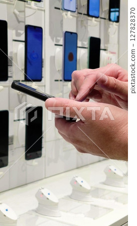 Hand of male buyer testing smartphone in electronics store. Choosing a phone in store. customer chooses a phone in store. 127828370