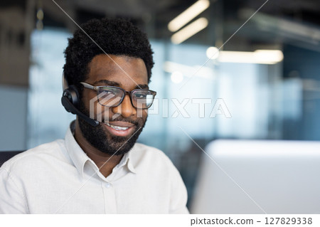 Portrait of a support worker, a man with a headset smiling and looking at the camera. A company employee close-up with a laptop inside the office 127829338
