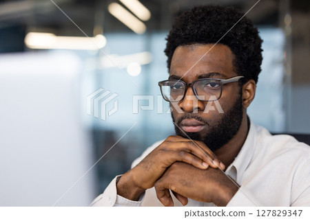 African American man businessman intensely focused on computer in office. Wearing glasses, displaying thoughtful expression. Represents concentration, work, technology. 127829347