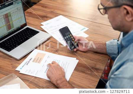 Man calculating household utility bills using smartphone and laptop. Managing household expenses and family budget concepts  127829711