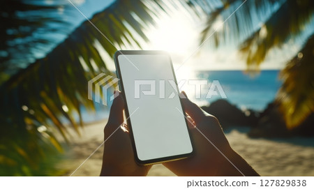Woman relaxing on a tropical beach at sunset, holding a smartphone with a blank screen, ideal for showcasing apps or websites, with swaying palm trees Woman relaxing on a tropical beach at sunset, holding a smartphone with a blank screen, ideal for showcasing apps or websites, with swaying palm trees 127829838