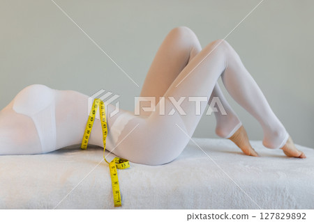 woman in a white suit for LPG massage holds a centimeter in her hands. Anti-cellulite body care concept. Gray background 127829892