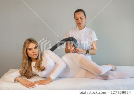 Woman in special white suit getting anti cellulite massage in a spa salon. LPG, and body contouring treatment in clinic.Reset body weight with LPG massage.  127829934