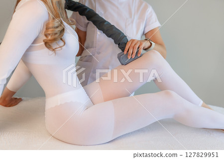 Woman in special white suit getting anti cellulite massage in a spa salon. LPG, and body contouring treatment in clinic.Reset body weight with LPG massage.  127829951