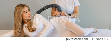 Woman in special white suit getting anti cellulite massage in a spa salon. LPG, and body contouring treatment in clinic.Reset body weight with LPG massage.  127829957