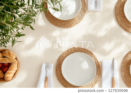 Elegant outdoor table setting with plates, cutlery, and bread on a light tablecloth 127830096