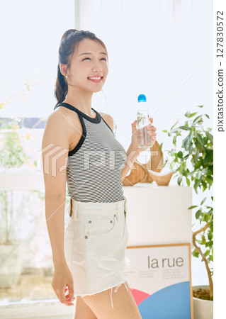 微笑的年輕女士在房間裡享用夏日清涼飲料 微笑的年輕女士在房間裡享用夏日清涼飲料 127830572