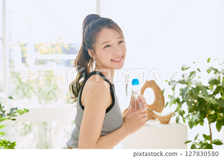 Smiling young woman enjoying summer refreshing drink in room Smiling young woman enjoying summer refreshing drink in room 127830580