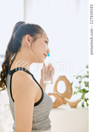 Smiling young woman enjoying summer refreshing drink in room Smiling young woman enjoying summer refreshing drink in room 127830583