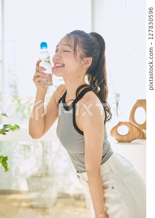 微笑的年輕女士在房間裡享用夏日清涼飲料 微笑的年輕女士在房間裡享用夏日清涼飲料 127830596