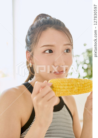 Smiling young woman holding corn in her hand in her room 127830597