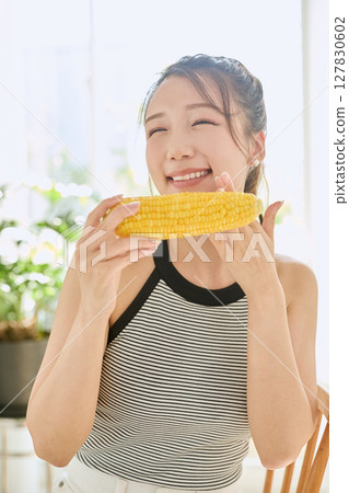 Smiling young woman holding corn in her hand in her room 127830602
