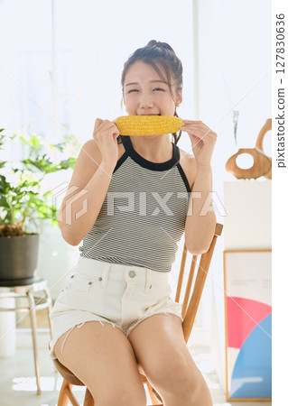 Smiling young woman holding corn in her hand in her room Smiling young woman holding corn in her hand in her room 127830636