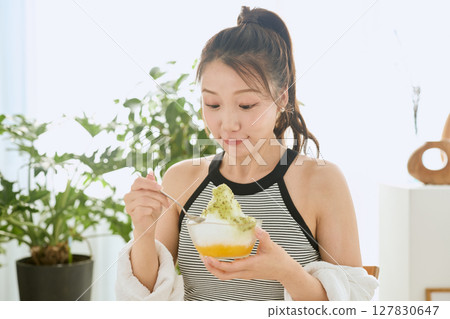 一位微笑的年輕女子吃刨冰享受夏日的生活方式 一位微笑的年輕女子吃刨冰享受夏日的生活方式 127830647