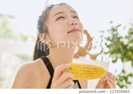 Smiling young woman holding corn in her hand in her room 127830665