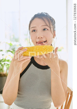 Smiling young woman holding corn in her hand in her room Smiling young woman holding corn in her hand in her room 127830668