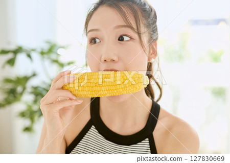 Smiling young woman holding corn in her hand in her room Smiling young woman holding corn in her hand in her room 127830669