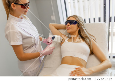 Hair removal procedure. Cropped shot of young fit woman client receiving laser hair removal procedure on body in beauty clinic. Women beauty and cosmetology concept 127830846