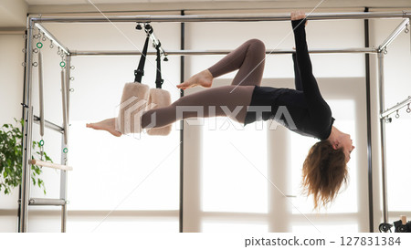 Caucasian woman doing aerial exercises on a reformer machine.  127831384