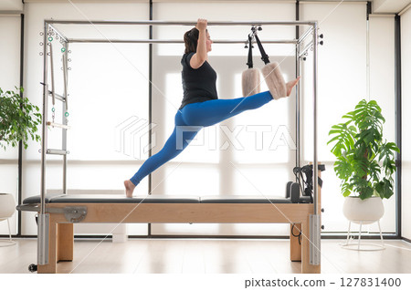 Focused Woman Practicing Pilates on a Reformer. Focused Woman Practicing Pilates on a Reformer. 127831400