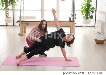 Overweight caucasian woman doing pilates exercises with personal trainer. Overweight caucasian woman doing pilates exercises with personal trainer. 127831405