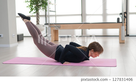 Concentrated woman doing pilates in studio alone. Concentrated woman doing pilates in studio alone. 127831406
