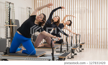 Three Asian women doing Pilates on a reformer. Three Asian women doing Pilates on a reformer. 127831420