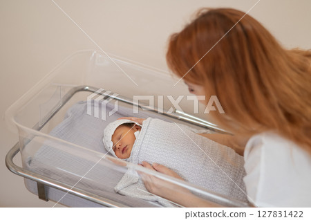 A young mother admires her newborn son in the maternity hospital. A young mother admires her newborn son in the maternity hospital. 127831422