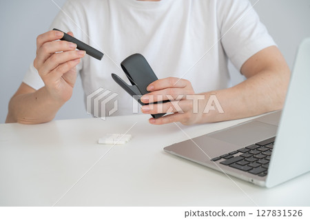 A woman smokes an electronic cigarette while working on a laptop. Tobacco heating system. A woman smokes an electronic cigarette while working on a laptop. Tobacco heating system. 127831526