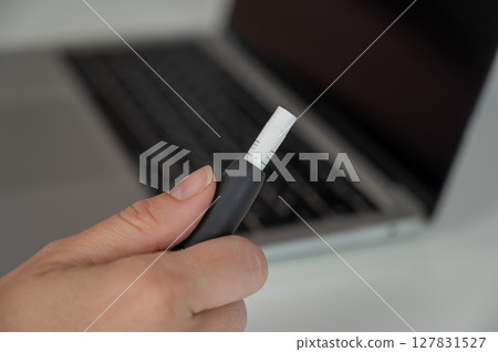 A woman smokes an electronic cigarette while working on a laptop. Tobacco heating system. 127831527