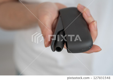 A woman takes a tobacco heating system out of a charger. Electronic cigarette. A woman takes a tobacco heating system out of a charger. Electronic cigarette. 127831548