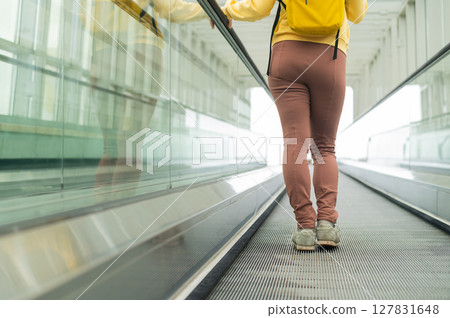 Rear view of a woman with a backpack moving on a travolator Rear view of a woman with a backpack moving on a travolator 127831648