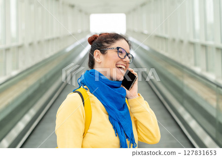 Happy woman stands on a travelator and talks on a cell phone Happy woman stands on a travelator and talks on a cell phone 127831653