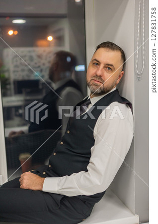 Thoughtful Caucasian man sitting on windowsill in office.  127831758