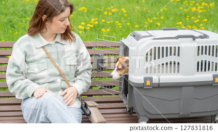 Caucasian woman traveling with dog. Owner sits on bench with Jack Russell Terrier in cage for safe travel. Caucasian woman traveling with dog. Owner sits on bench with Jack Russell Terrier in cage for safe travel. 127831816