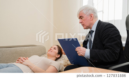 Caucasian woman lies on a couch at a reception with a psychotherapist. An elderly man works as a psychiatrist Caucasian woman lies on a couch at a reception with a psychotherapist. An elderly man works as a psychiatrist 127831886