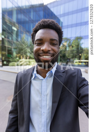 A happy African-American businessman in a suit stands outside a modern office building, exuding confidence and success. 127832920