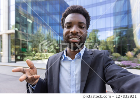 An african american man is on a video call, looking towards the camera and gesturing with his hands outside a building 127832921