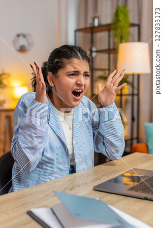 Aggressive young Indian woman screams yells from stress tension panic sitting at home office desk Aggressive young Indian woman screams yells from stress tension panic sitting at home office desk 127833173