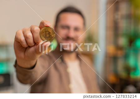 Portrait of happy young male freelancer trader showing golden bitcoins sitting at home office table Portrait of happy young male freelancer trader showing golden bitcoins sitting at home office table 127833214