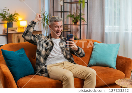 Surprised excited man winner holding smartphone reading good news amazed by online game casino win 127833222