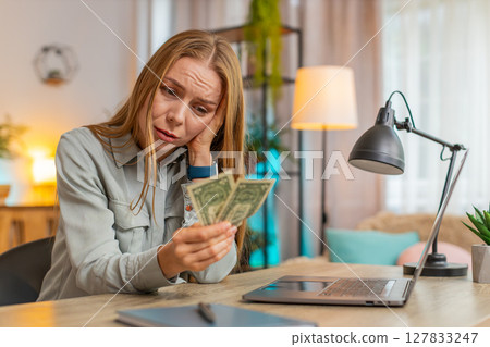Upset Caucasian woman freelancer counting dollar cash insufficient amount of money sitting at table Upset Caucasian woman freelancer counting dollar cash insufficient amount of money sitting at table 127833247