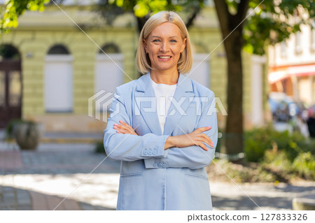 Happy mature Caucasian businesswoman lady standing arms crossed looking at camera on city street 127833326