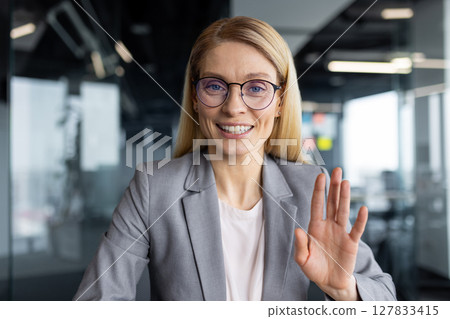 Webcam view of successful joyful businesswoman talking to colleagues and partners using laptop and video call. Woman looking at camera while sitting inside office at workplace, online meeting. 127833415