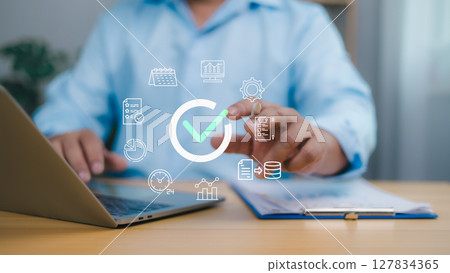 Person using a laptop with a large checkmark icon and business related icons calendar, graph, symbolizing process completion, quality assurance, efficient management, and successful project delivery. Person using a laptop with a large checkmark icon and business related icons calendar, graph, symbolizing process completion, quality assurance, efficient management, and successful project delivery. 127834365
