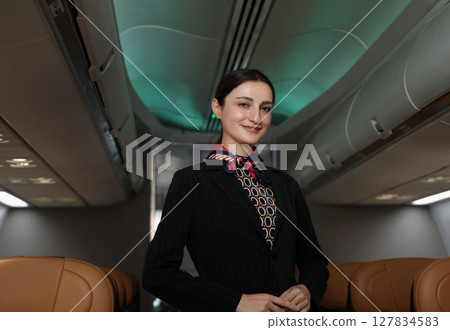 Smiling flight attendant in uniform welcomes and guides passengers aboard a modern airplane. 127834583