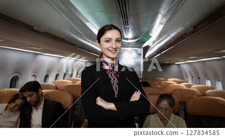 Smiling flight attendant in uniform welcomes and guides passengers aboard a modern airplane. Smiling flight attendant in uniform welcomes and guides passengers aboard a modern airplane. 127834585